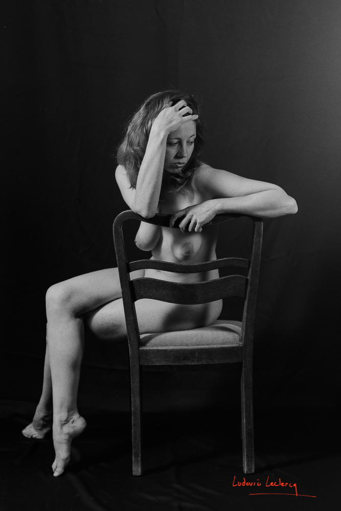 Nu artistique. L'art de poser nue. Femme assise sur une chaise, photographie argentique en noir et blanc.