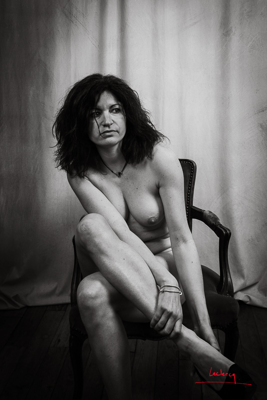 Femme nue assise dans le studio retirant sa chaussure, photographie en noir et blanc.