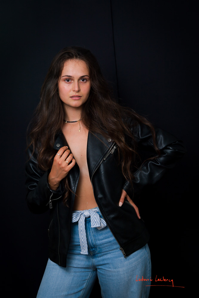 Une jeune femme pose en studio. Elle porte un blouson en cuir noir.