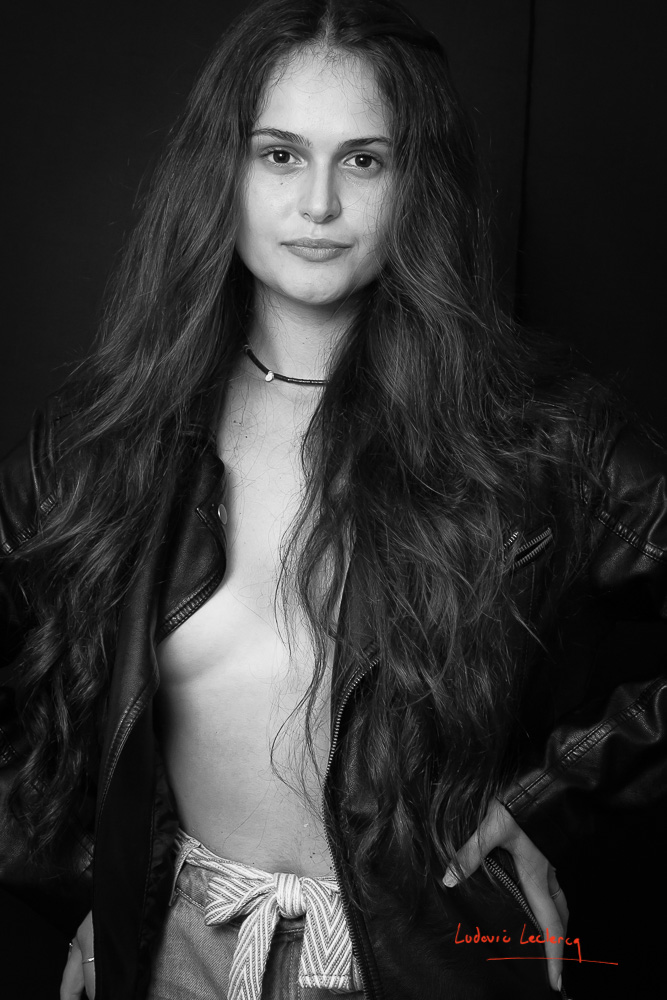 Jeune femme photographiée en noir et blanc. Elle porte un blouson en cuir à même la peau.