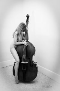 Une femme pose nue debout avec sa contrebasse, photographie en noir et blanc.