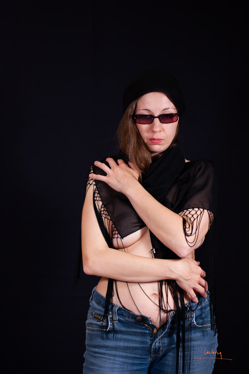 Photo de charme sur fond noir réalisée en studio. La femme porte des lunettes de soleil.