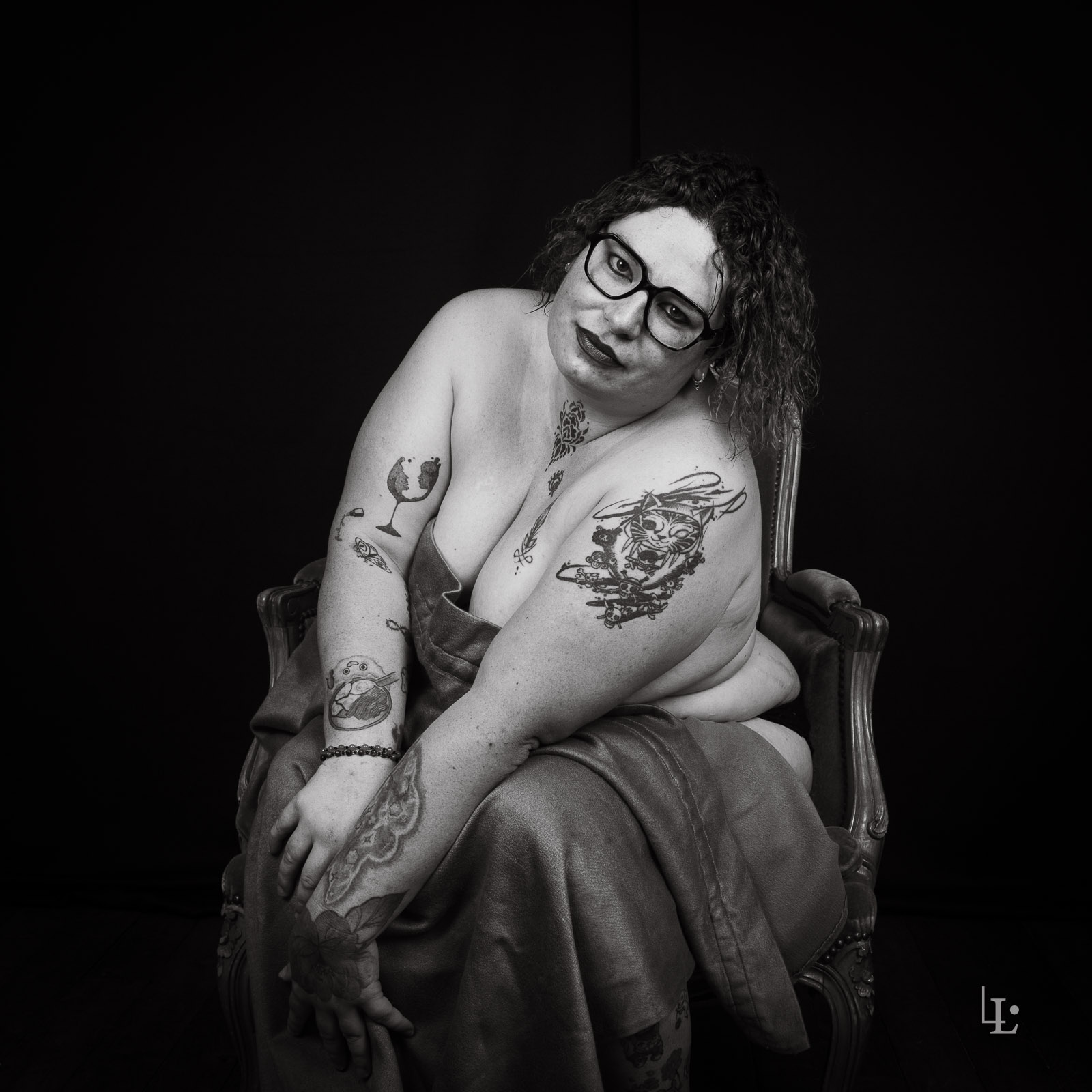 Une femme pose assise dans un fauteuil Louis XV en studio. Séance photo boudoir en noir et blanc à Chantilly dans l'Oise.